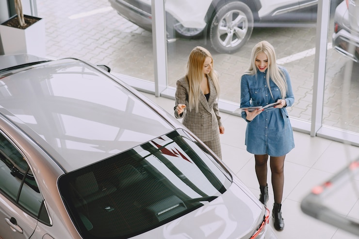 Foto gratuito señoras en un salón de autos. mujer comprando el coche. mujer elegante con un vestido azul. el gerente ayuda al cliente.