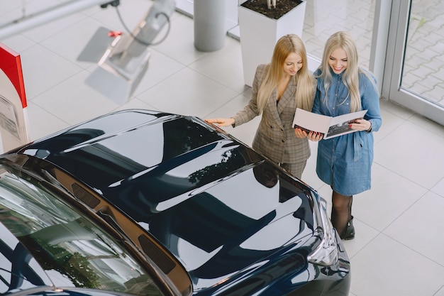 Señoras en un salón de autos. Mujer comprando el coche. Mujer elegante con un vestido azul. El gerente ayuda al cliente.