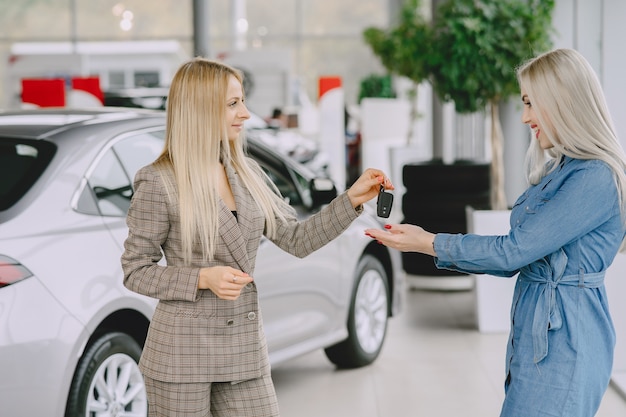 Señoras en un salón de autos. Mujer comprando el coche. Mujer elegante con un vestido azul. Gerente entrega llaves al cliente.