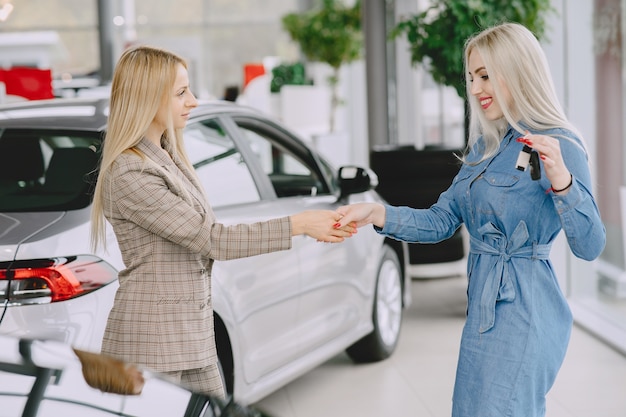 Señoras en un salón de autos. Mujer comprando el coche. Mujer elegante con un vestido azul. Gerente entrega llaves al cliente.