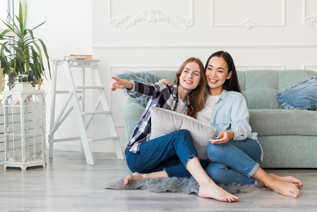 Señoras sonrientes que se sientan descalzo en piso