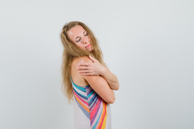 Foto gratuita señorita abrazándose a sí misma en vestido de verano y buscando pacífica.
