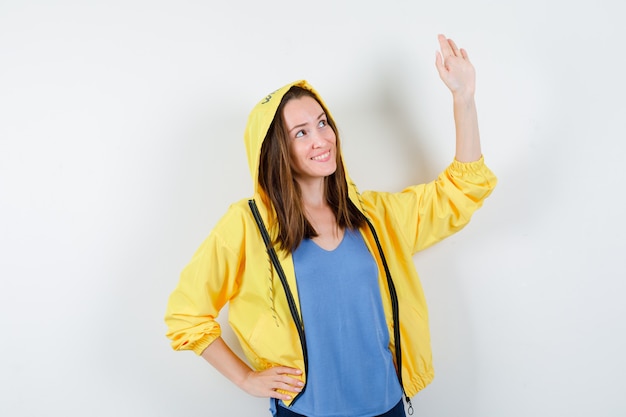 Señorita agitando la mano para decir adiós en camiseta, chaqueta y mirando alegre, vista frontal.