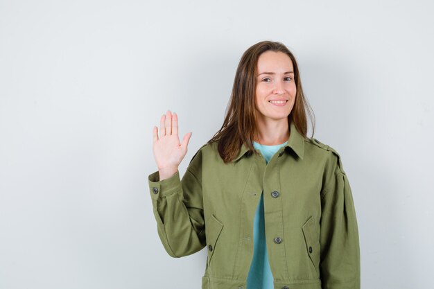 Señorita agitando la mano para saludar en camiseta, chaqueta y lucir linda. vista frontal.