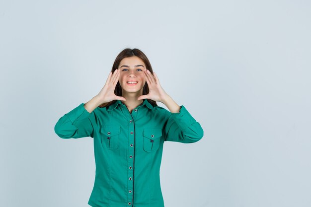 Señorita anunciando algo o diciendo un secreto en camisa verde y mirando alegre, vista frontal.