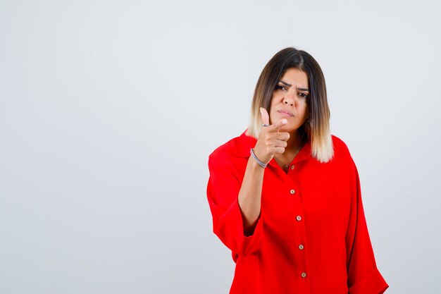 Señorita apuntando hacia adelante con camisa roja de gran tamaño y mirando serio, vista frontal.