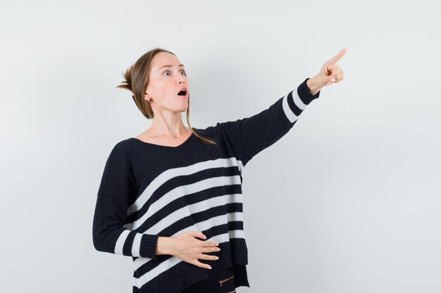 Señorita apuntando hacia afuera en camisa casual y mirando sorprendido