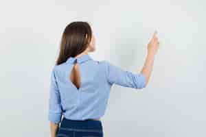 Foto gratuita señorita apuntando a algo en la pared con camisa azul