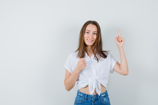 Señorita apuntando hacia arriba en blusa blanca, vista frontal.