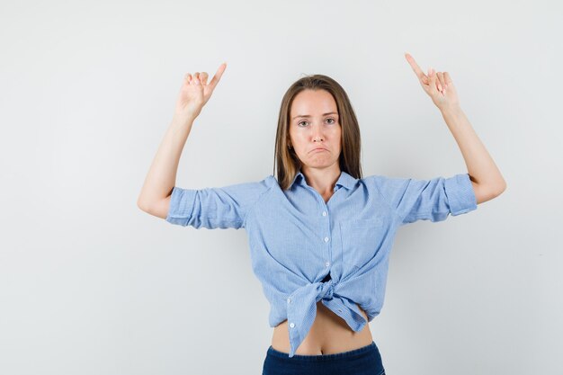 Señorita apuntando hacia arriba con camisa azul, pantalones y mirando decepcionado