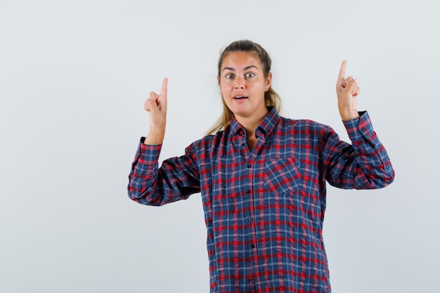 Señorita apuntando hacia arriba con camisa a cuadros y mirando feliz. vista frontal.