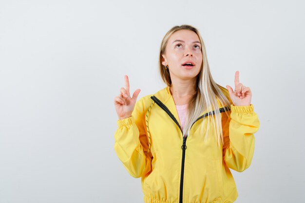 Señorita apuntando hacia arriba en camiseta, chaqueta y mirando perplejo