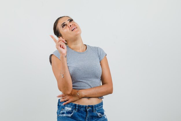 Señorita apuntando hacia arriba en camiseta, pantalones cortos y luciendo esperanzada.