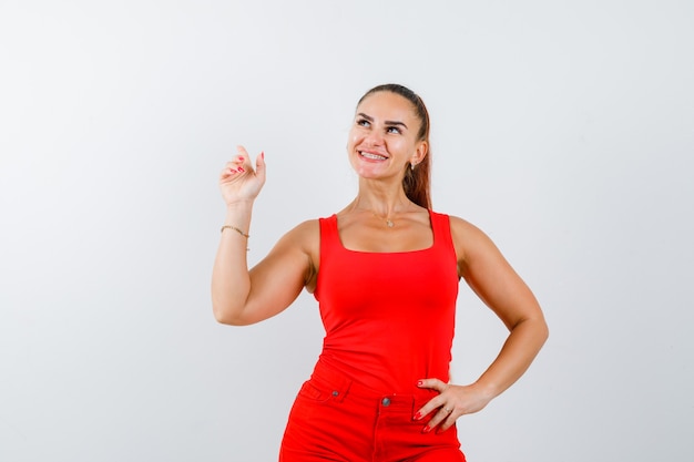 Señorita apuntando hacia arriba en camiseta roja, pantalón rojo y mirando alegre. vista frontal.