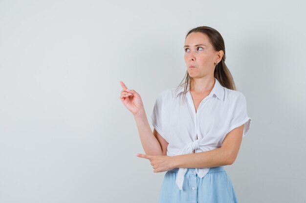 Señorita apuntando hacia arriba y a un lado en blusa y falda y mirando vacilante