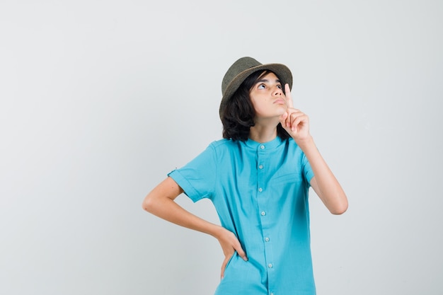 Señorita apuntando hacia arriba mientras escucha con camisa azul, sombrero y mirando enfocado.