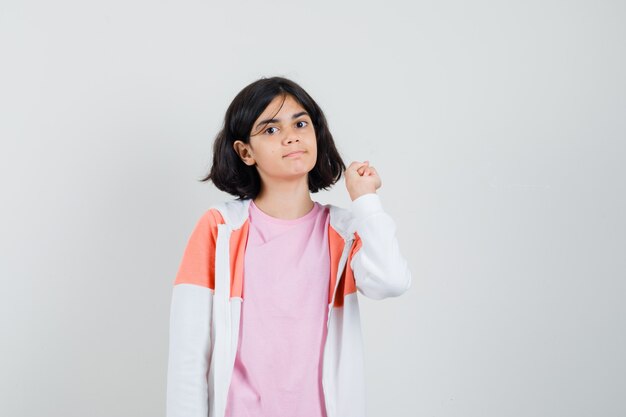 Señorita apuntando hacia atrás en chaqueta, camisa rosa y mirando tranquila.