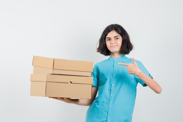 Señorita apuntando a cajas en camisa azul y mirando listo.