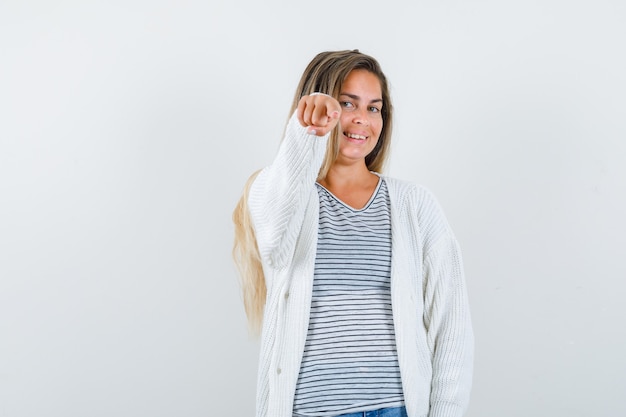 Señorita apuntando a la cámara en camiseta, chaqueta y mirando alegre, vista frontal.