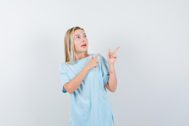 Señorita apuntando a la esquina superior derecha en camiseta y mirando confiado aislado