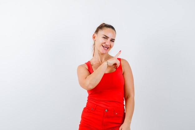 Señorita apuntando a la esquina superior derecha con camiseta roja, pantalón rojo y aspecto alegre. vista frontal.