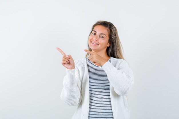 Señorita apuntando a la esquina superior izquierda en camiseta, chaqueta y luciendo esperanzada. vista frontal.