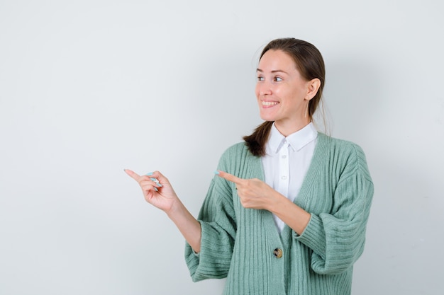 Foto gratuita señorita apuntando a la izquierda, mirando a un lado en blusa, chaqueta de punto y mirando jovial, vista frontal.