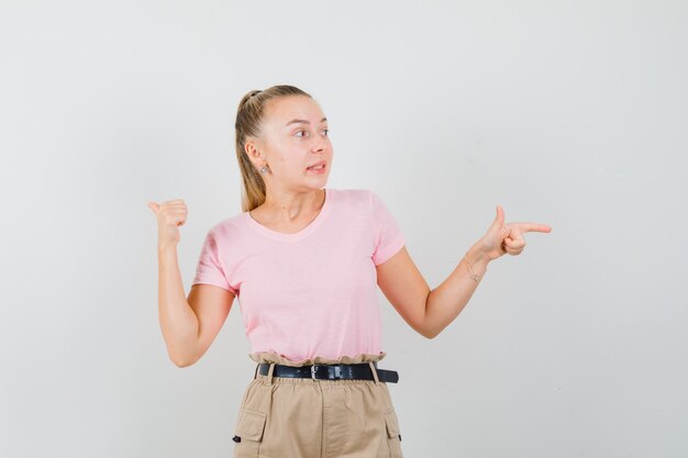 Señorita apuntando hacia un lado y hacia atrás en camisetas y pantalones y mirando indecisa