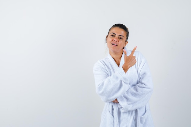 Señorita apuntando a un lado en bata de baño y mirando alegre