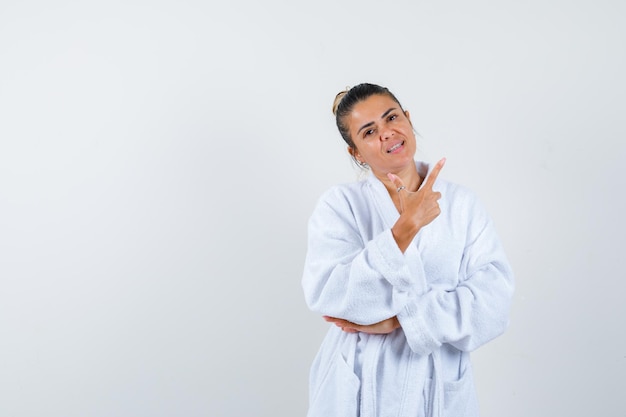 Señorita apuntando a un lado en bata de baño y mirando alegre