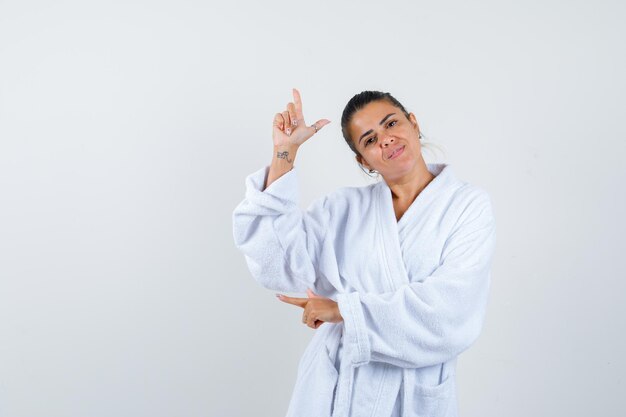 Señorita apuntando a un lado en bata de baño y mirando alegre