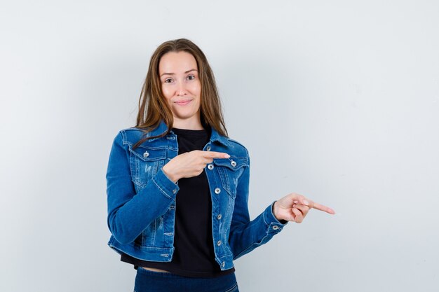 Señorita apuntando a un lado en blusa, chaqueta y mirando confiado, vista frontal.