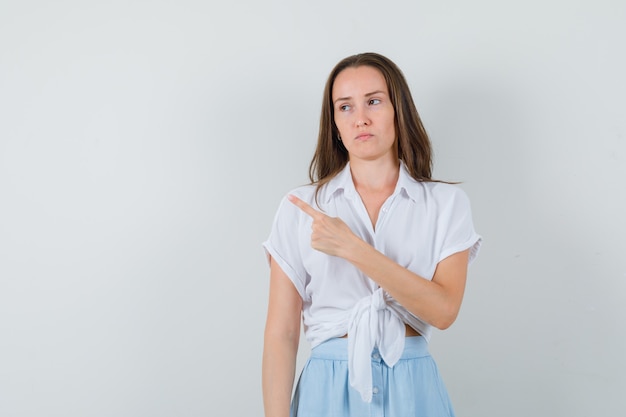 Señorita apuntando a un lado en blusa y falda y mirando descontento