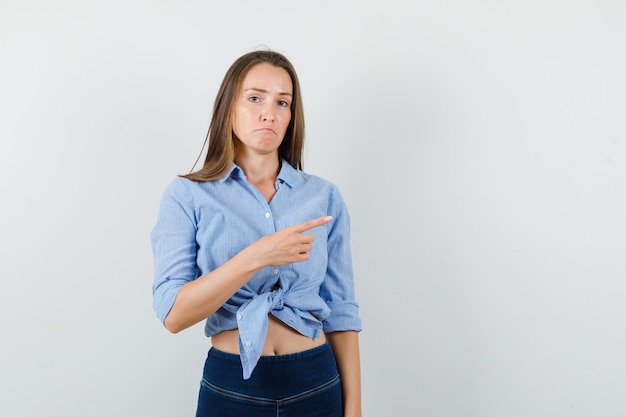 Señorita apuntando a un lado con camisa azul, pantalones y mirando ofendido.