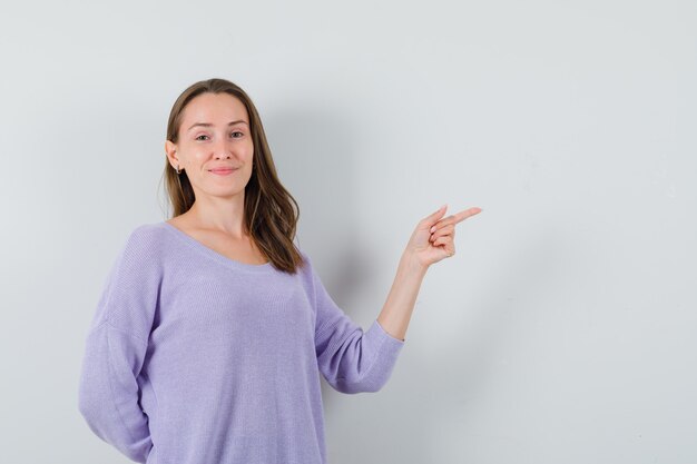 Señorita apuntando a un lado en camisa casual y mirando feliz