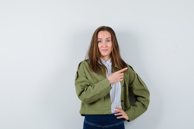 Señorita apuntando a un lado en camisa, chaqueta y mirando alegre, vista frontal.