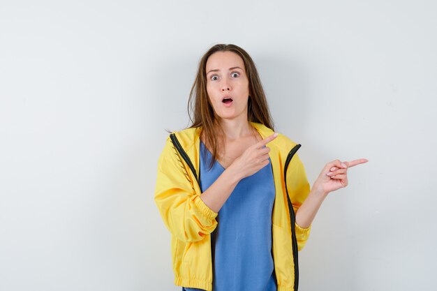 Señorita apuntando a un lado en camiseta, chaqueta y mirando sorprendido, vista frontal.