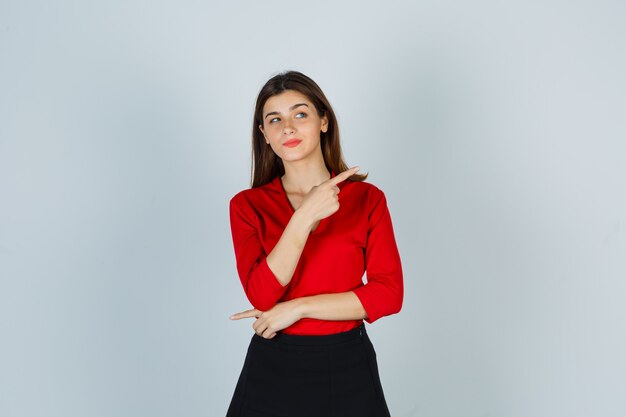 Señorita apuntando hacia el lado derecho en blusa roja, falda y luciendo linda