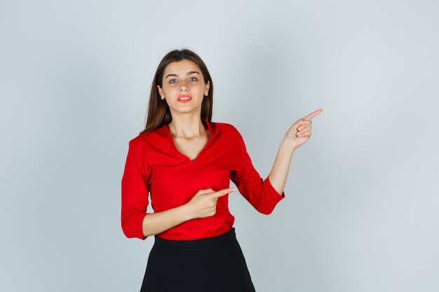 Foto gratuita señorita apuntando hacia el lado derecho en blusa roja, falda y mirando feliz