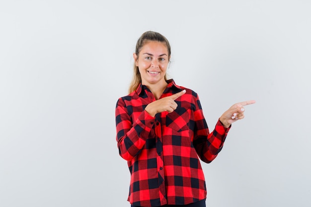 Señorita apuntando hacia el lado derecho en camisa casual y mirando alegre, vista frontal.