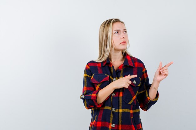 Señorita apuntando hacia el lado derecho con camisa a cuadros y mirando pensativo, vista frontal.