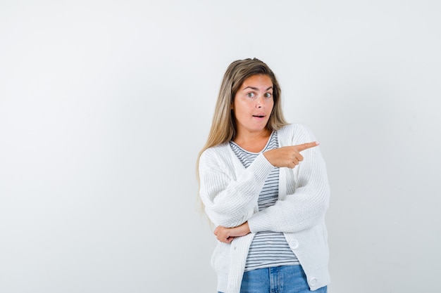 Señorita apuntando hacia el lado derecho en camiseta, chaqueta y mirando curiosa, vista frontal.