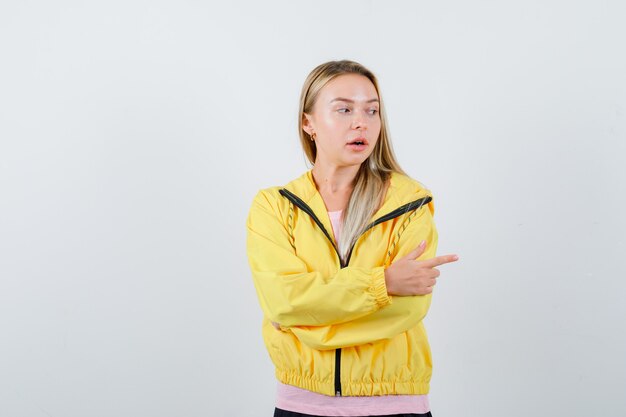 Señorita apuntando hacia el lado derecho en camiseta, chaqueta y mirando perplejo