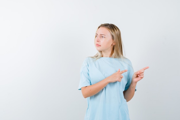 Señorita apuntando hacia el lado derecho en camiseta y mirando vacilante, vista frontal.