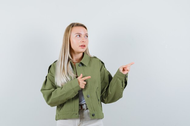 Señorita apuntando hacia el lado derecho en chaqueta, pantalón y mirando pensativa, vista frontal.