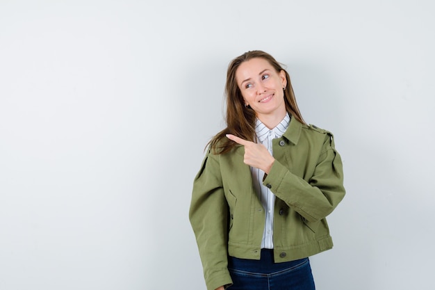 Señorita apuntando hacia el lado izquierdo en camisa, chaqueta y mirando encantador, vista frontal.