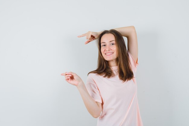 Señorita apuntando hacia el lado izquierdo en camiseta rosa y mirando confiada