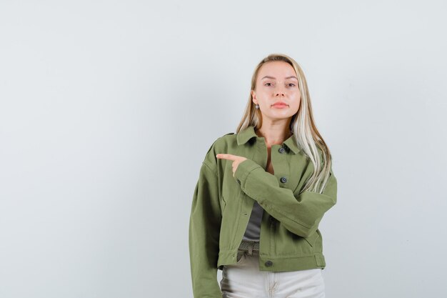 Señorita apuntando hacia el lado izquierdo en chaqueta, pantalón y mirando confiada, vista frontal.