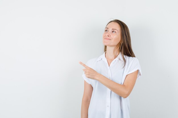 Señorita apuntando hacia otro lado mientras sonríe en blusa blanca y mira con cuidado