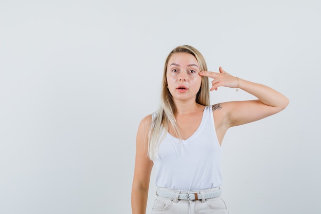 Señorita apuntando a su ojo en blusa blanca y mirando espacio enfocado para texto